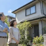 自宅の外壁と屋根を見上げる夫婦（イメージ）