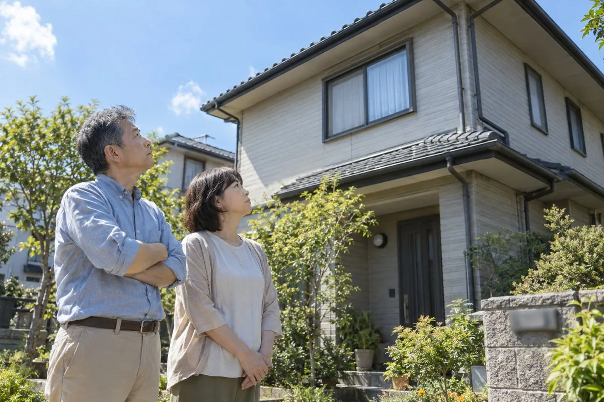 自宅の外壁と屋根を見上げる夫婦（イメージ）